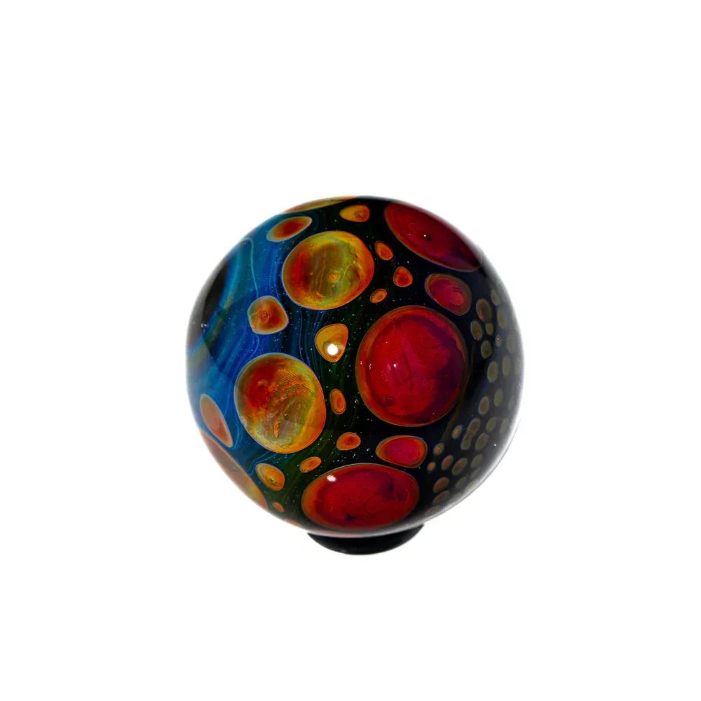 Hand-blown glass marble with vibrant red, orange, and blue bubble patterns on black