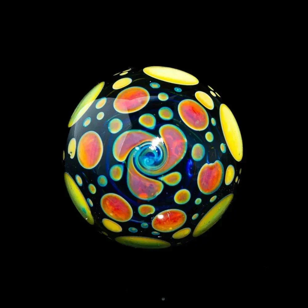 Colorful glass marble with vibrant yellow and red hobnail patterns on a dark background