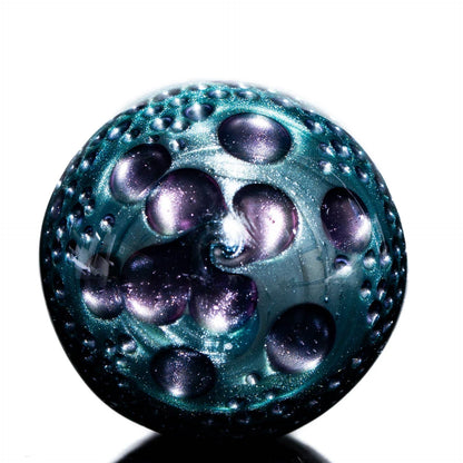 Iridescent purple and teal glass marble with textured, bubble-like patterns on a white background.