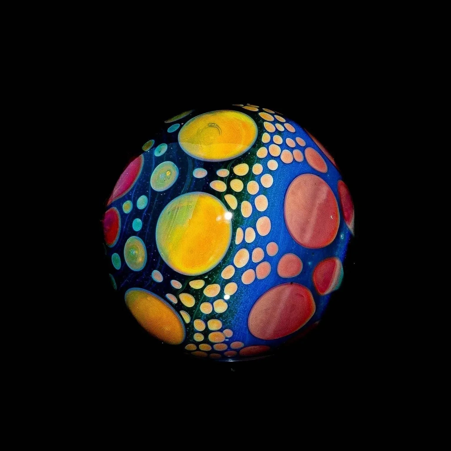 Hand-blown glass marble with blue base, yellow and orange hobnail dot patterns, on black background