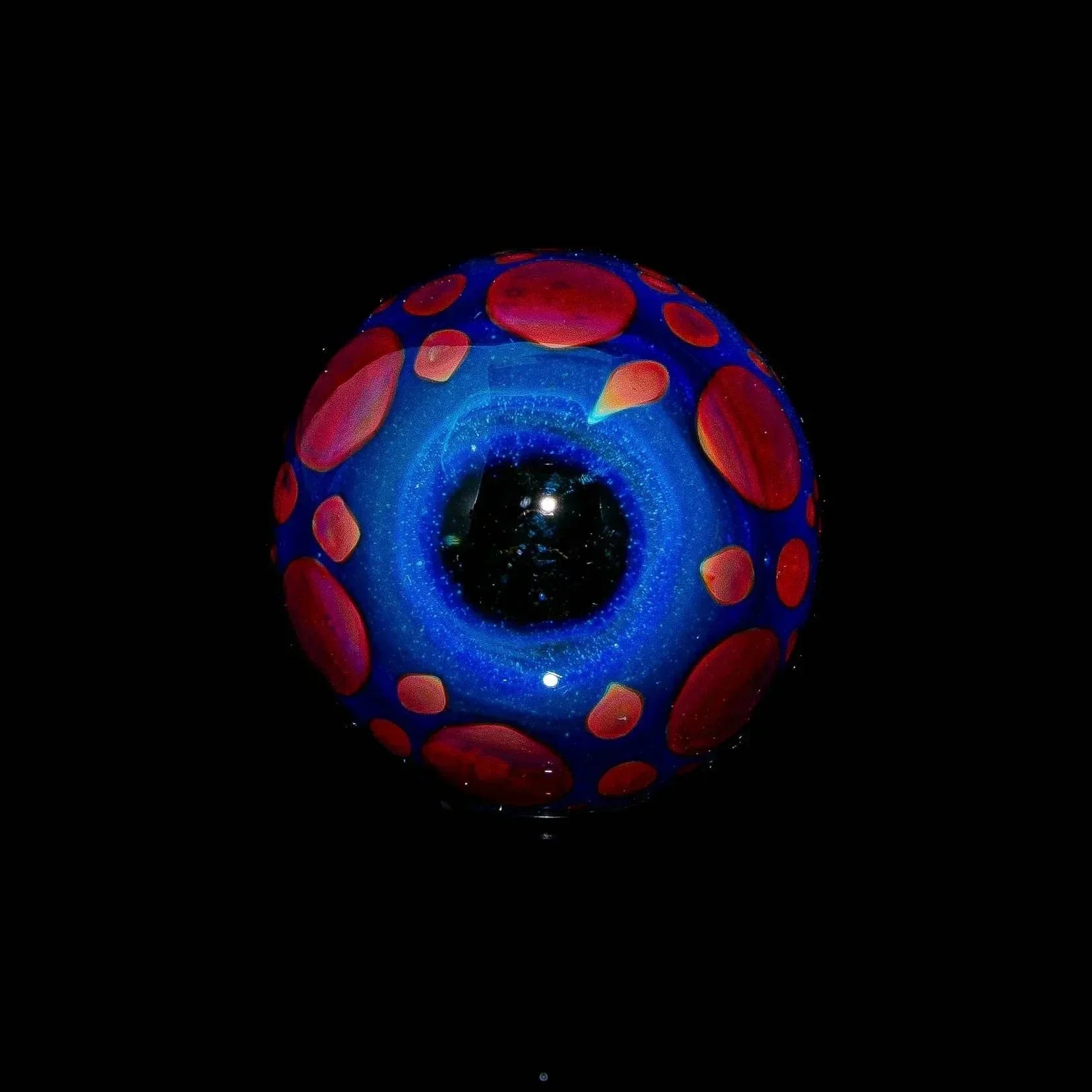 Blue and green glass marble with red hobnail accents on black background