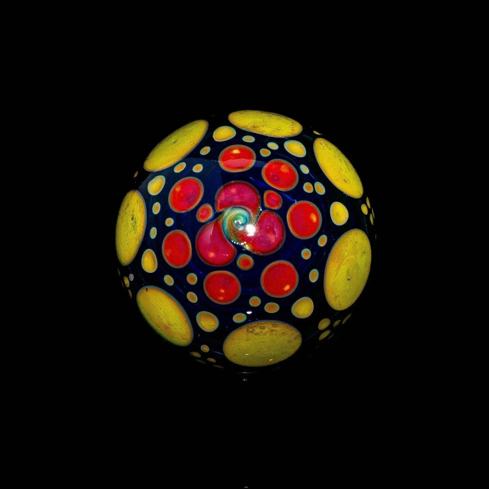 Blue glass marble with yellow and red hobnail dots on black background.