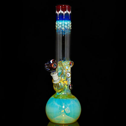 Colorful glass water pipe with fumed design, decorative marbles, and patterned bowl on black background.