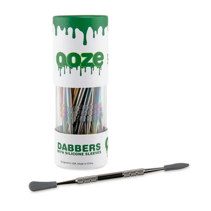 Ooze dabbers with silicone sleeves in a display container, rainbow metal tool shown
