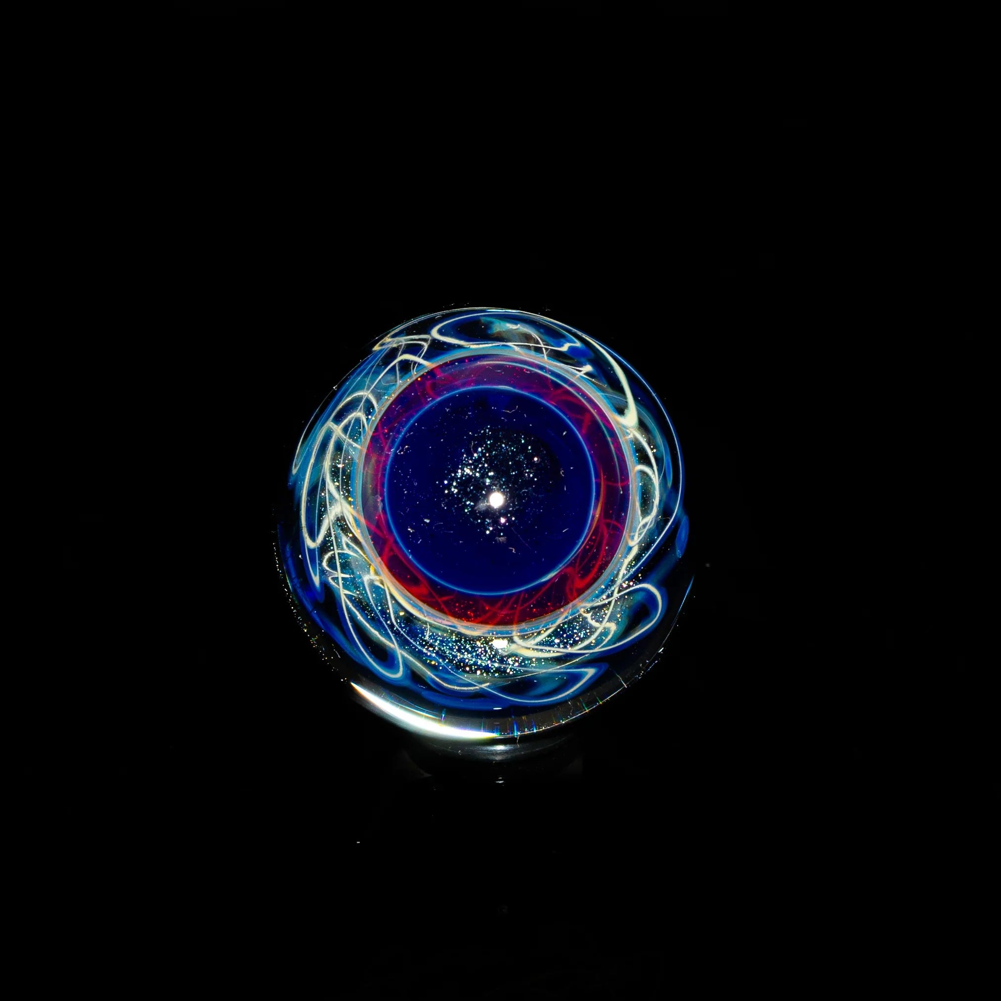Colorful heady glass marble with swirling blue, red, and white patterns on black background