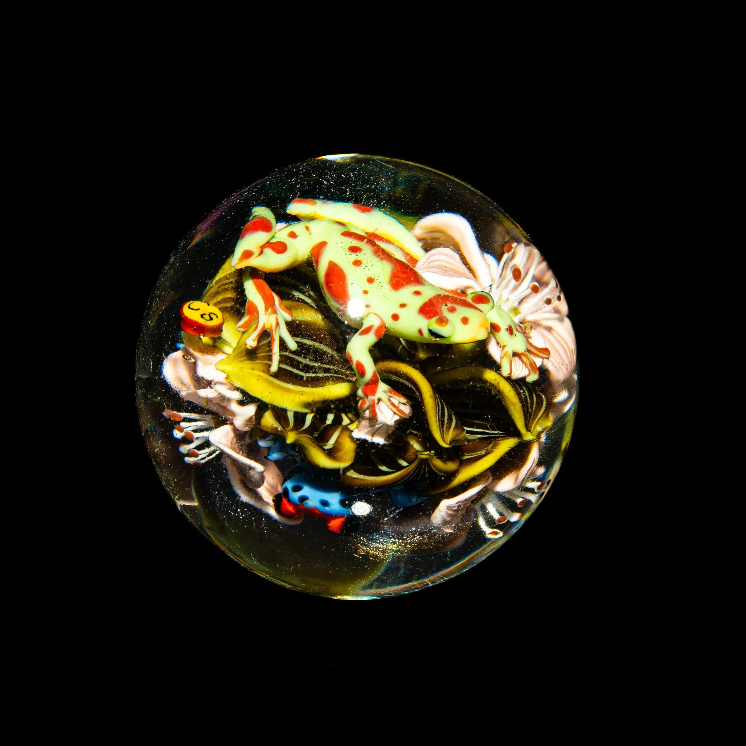Handcrafted glass marble with colorful frog and intricate floral designs on black background