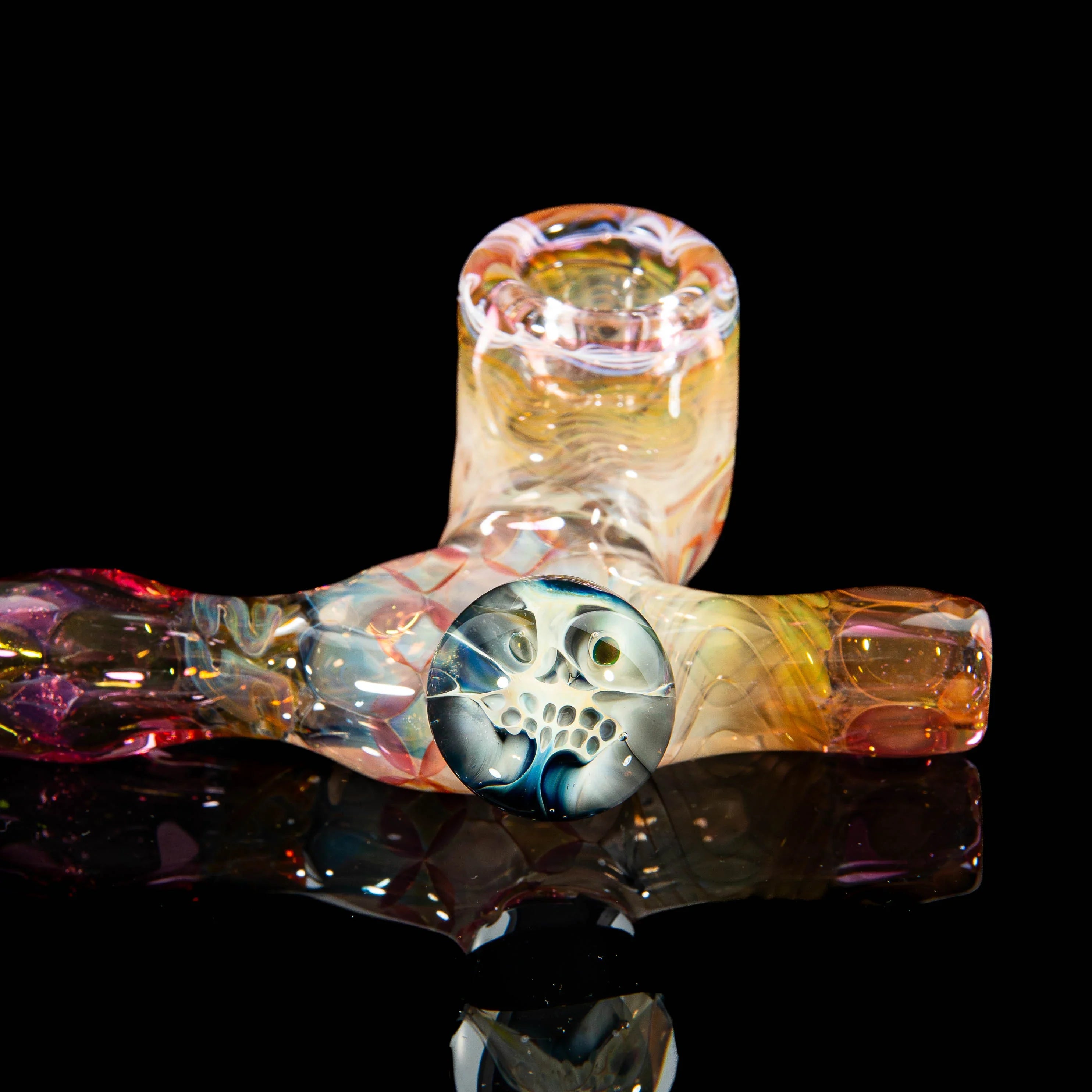Heady glass hand pipe with intricate colorful design and detailed face accent on black background