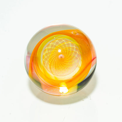 Handcrafted glass marble with vibrant orange and yellow spiral design on white background