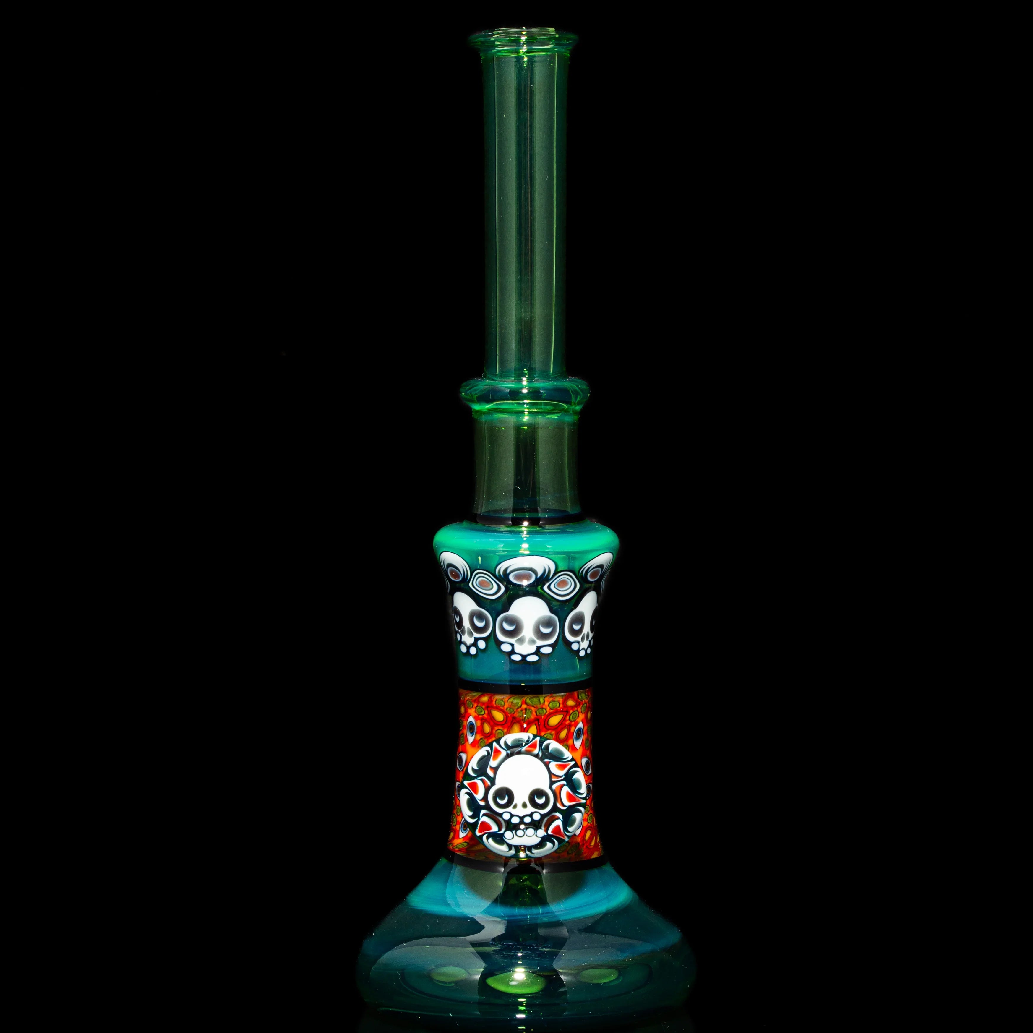 Heady glass water pipe with colorful skull designs and turquoise accents on black background