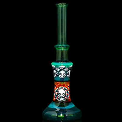 Heady glass water pipe with colorful skull designs and turquoise accents on black background