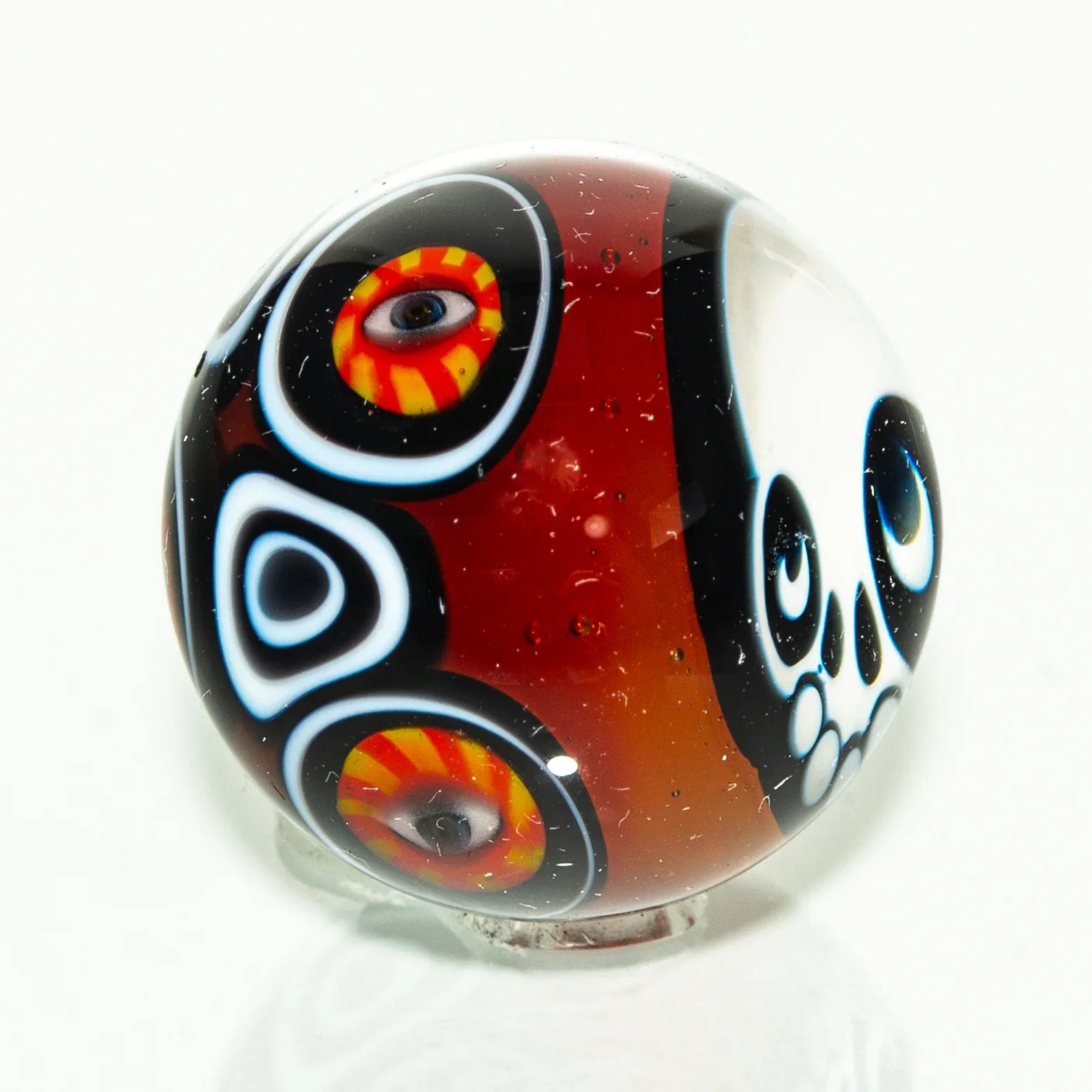 Handcrafted glass marble with skull and colorful eye designs on a red and black background