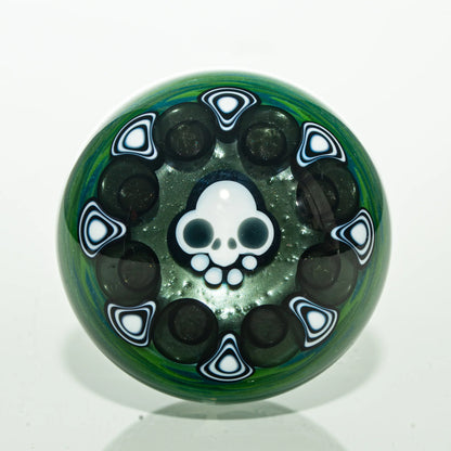 Handcrafted glass marble with skull design and black white accents on green background