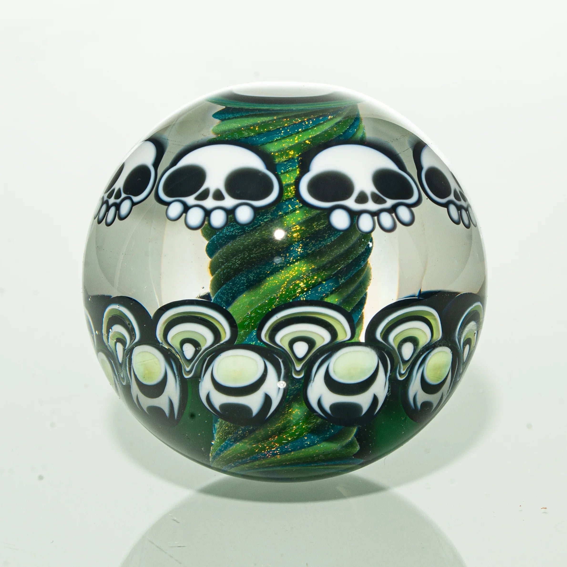 Handmade glass marble with white skull designs and green spiral core on a white background