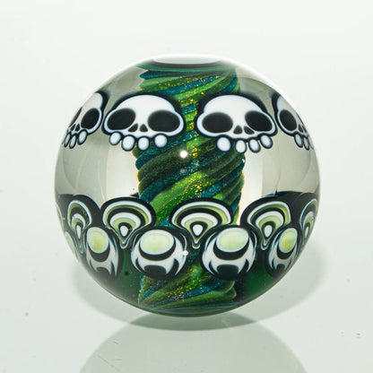 Handmade glass marble with white skull designs and green spiral core on a white background