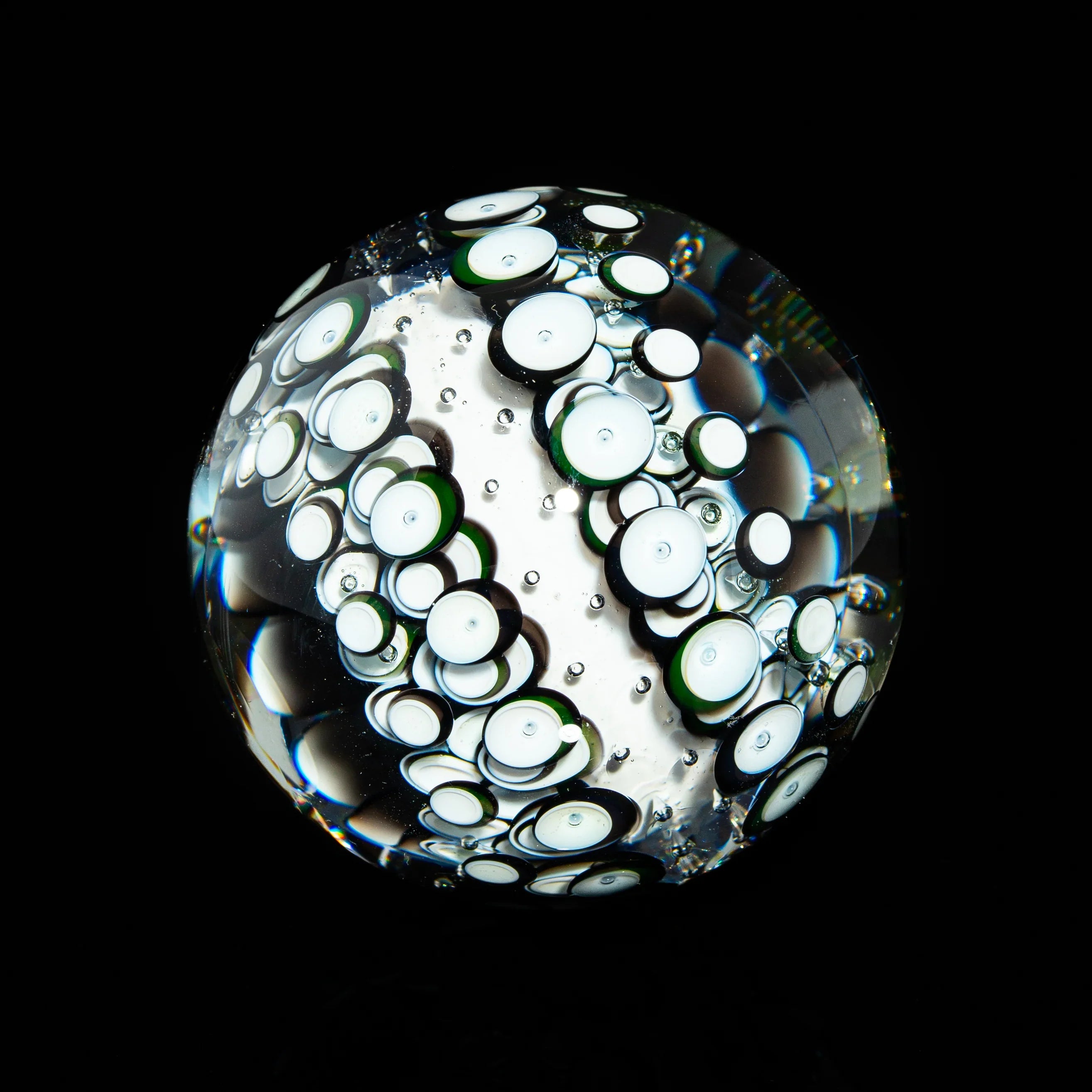 Handcrafted glass marble with intricate white and green bubble patterns on black background