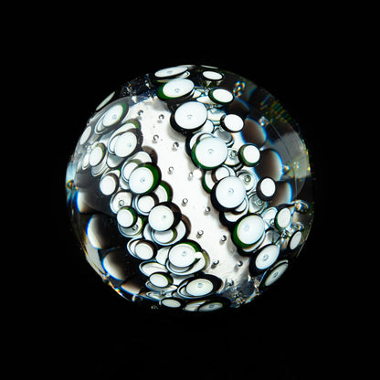 Handcrafted glass marble with intricate white and green bubble patterns on black background