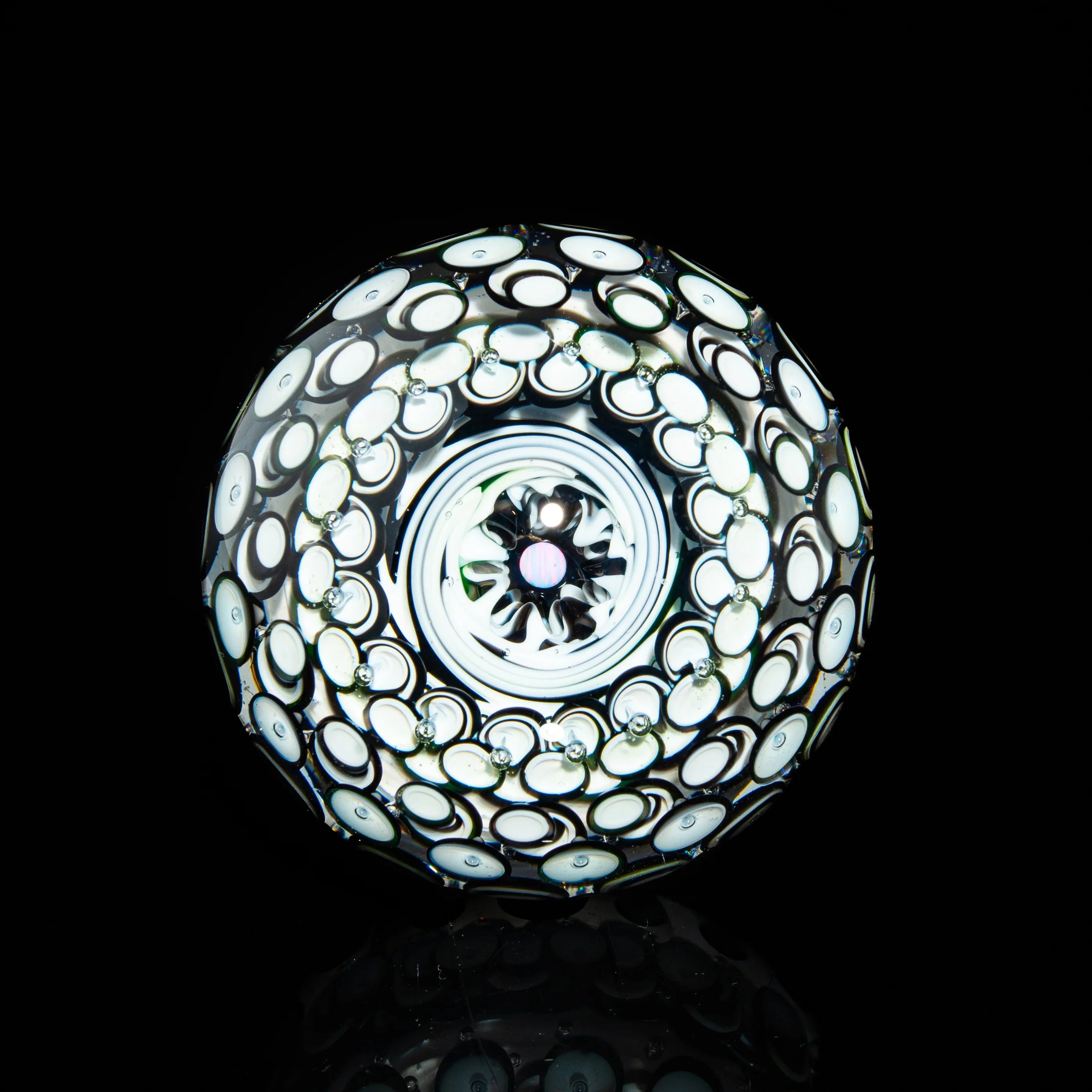 Handcrafted glass marble with intricate white and black swirling patterns on black background