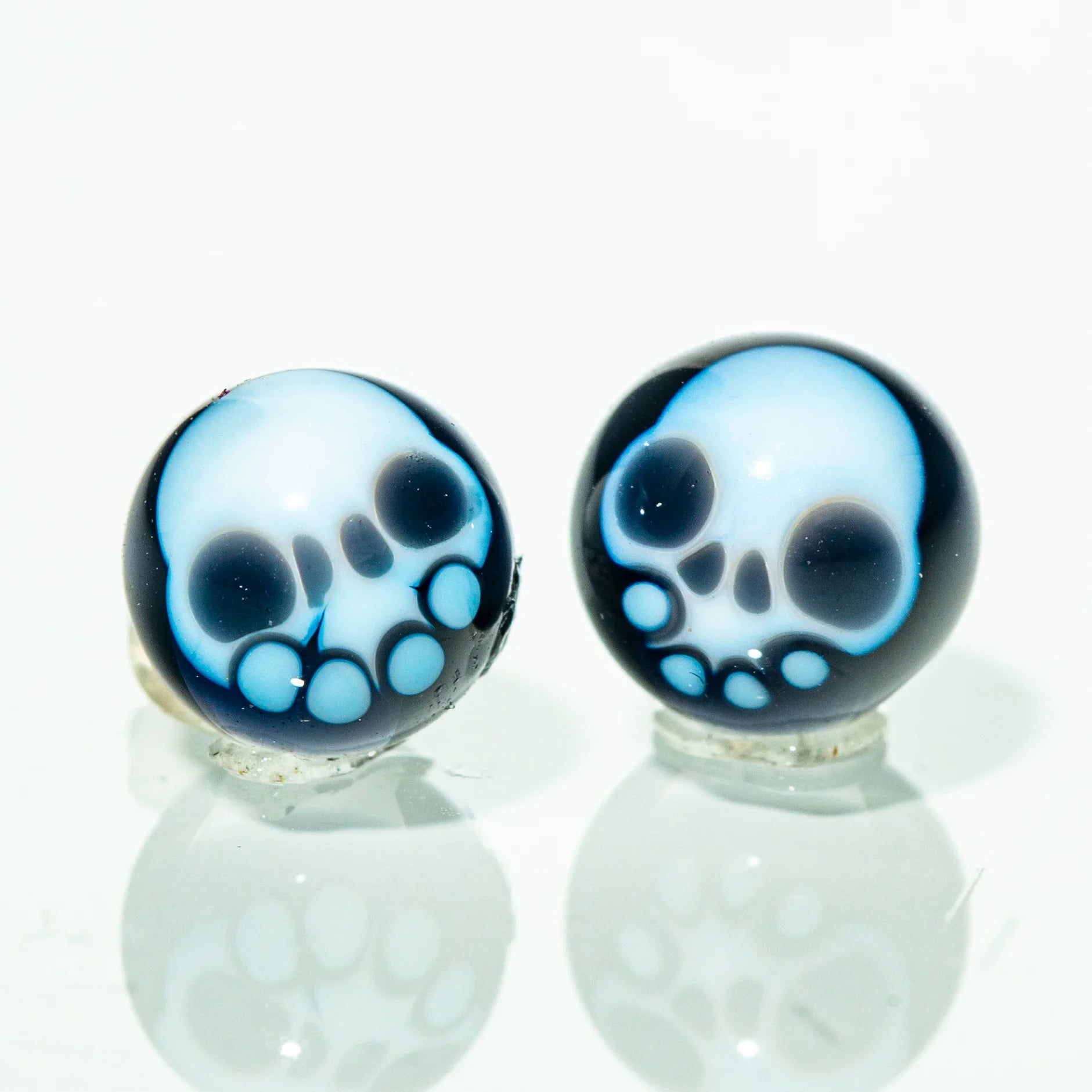 Two glass skull terp pearls with blue and white design on a reflective surface