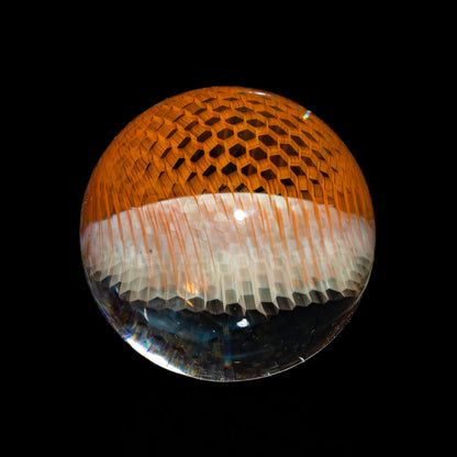 Handcrafted glass marble with honeycomb pattern and orange accents on black background