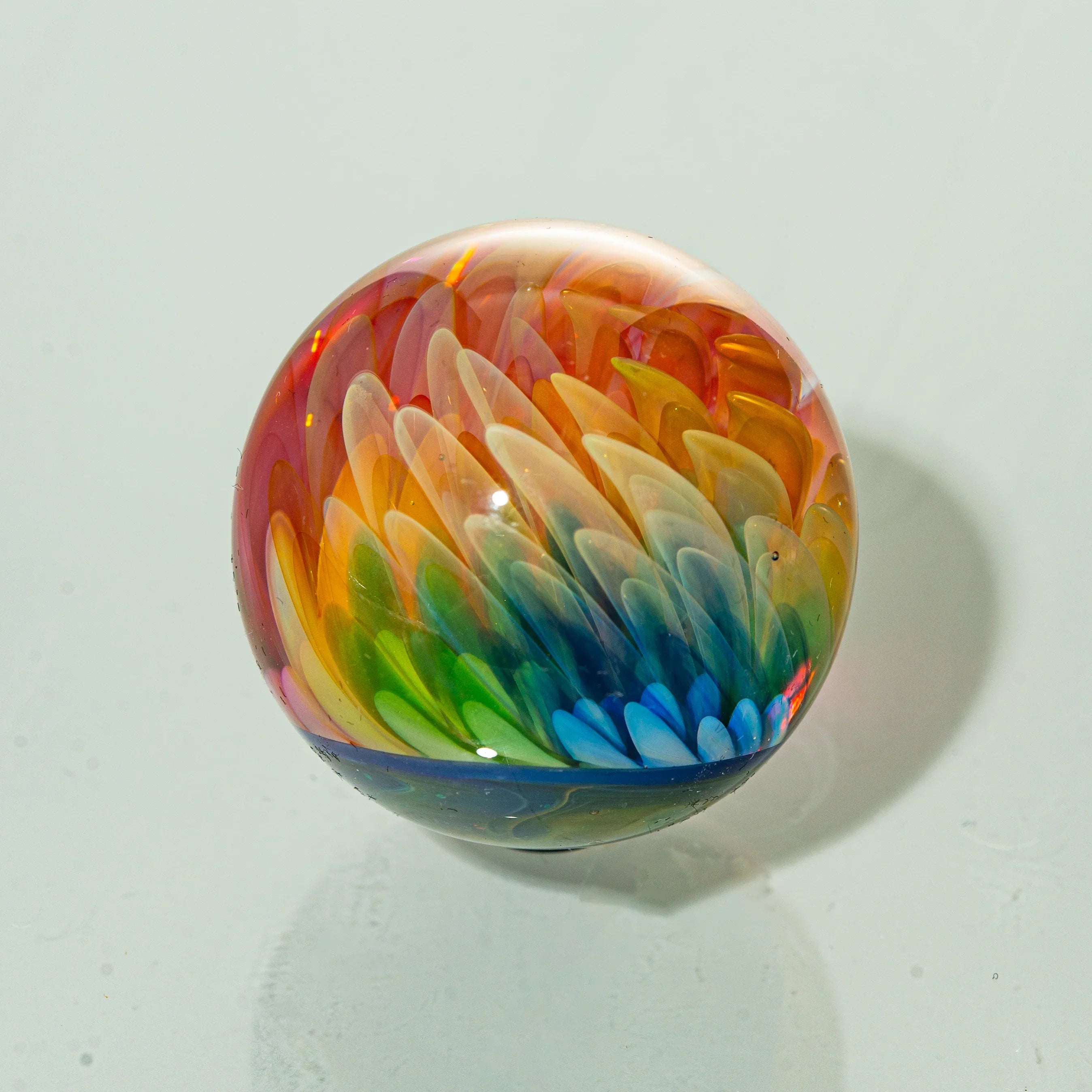 Handcrafted glass marble with intricate rainbow feather design