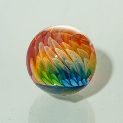 Handcrafted glass marble with intricate rainbow feather design