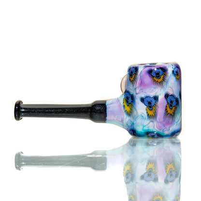 Colorful glass hand pipe with cartoon bear designs and black stem on reflective surface