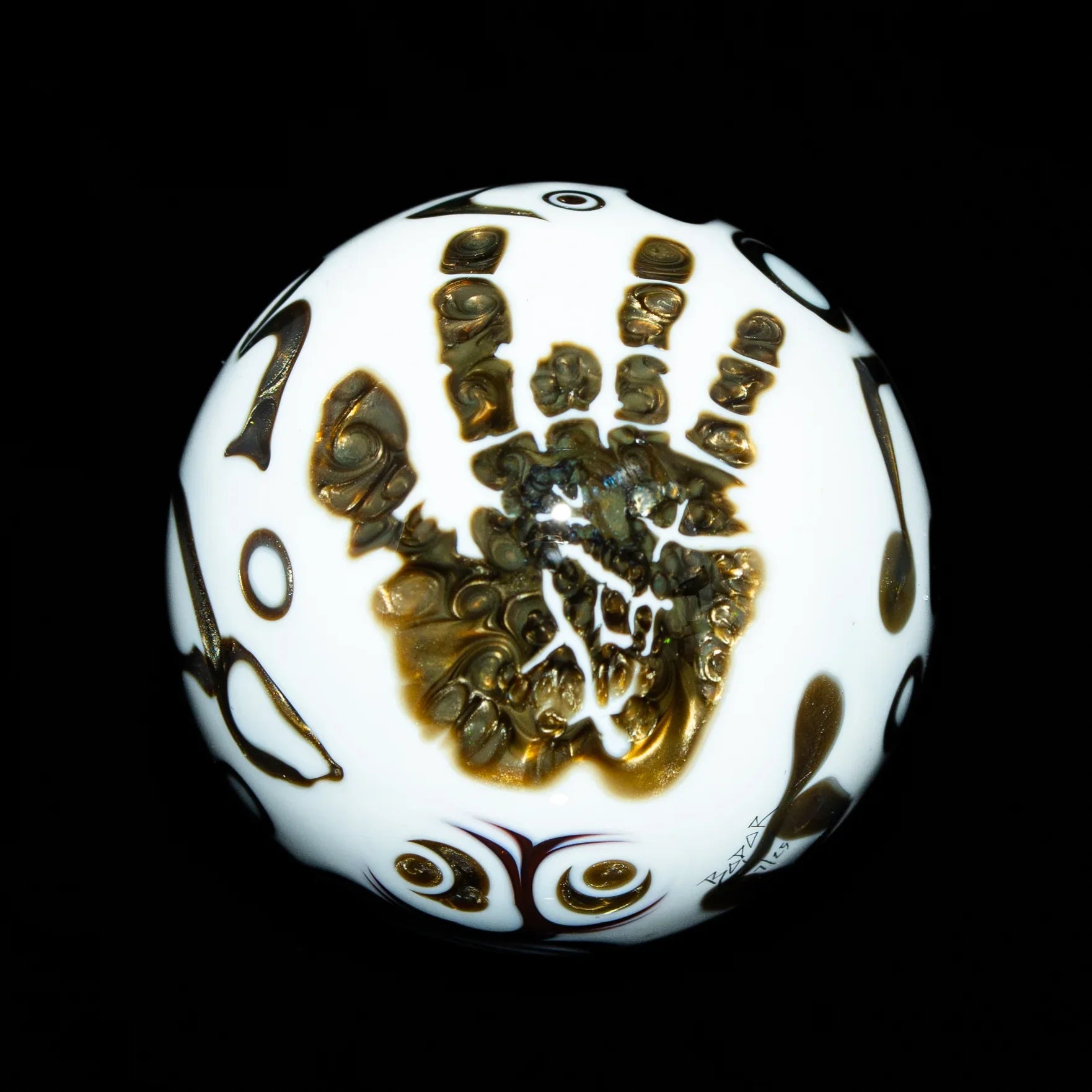White glass marble with intricate gold handprint and patterned designs on black background