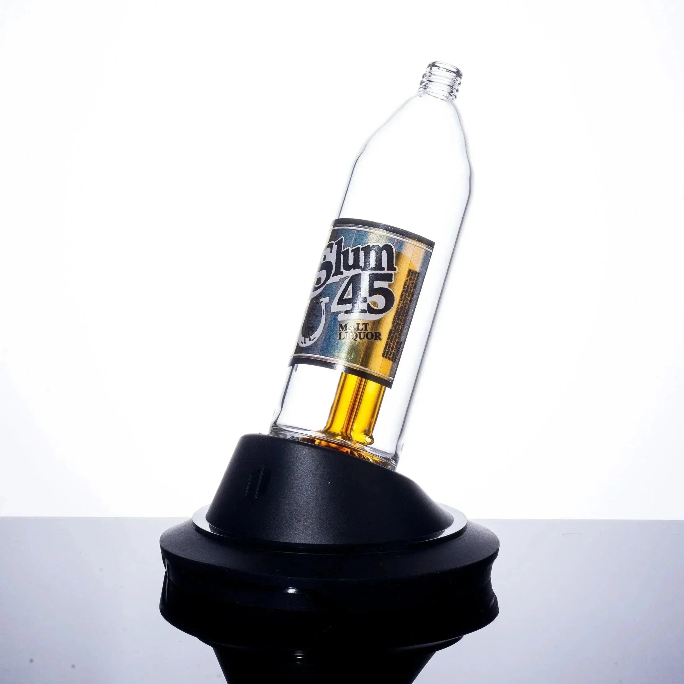 Slum 45 malt liquor bottle on black stand, clear glass with golden liquid, minimalist white background