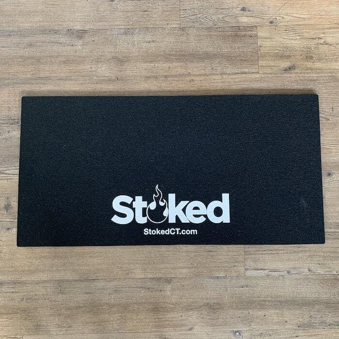Black mood mat on a wooden background; white Stoked logo in bottom center, includes stokedCT.com