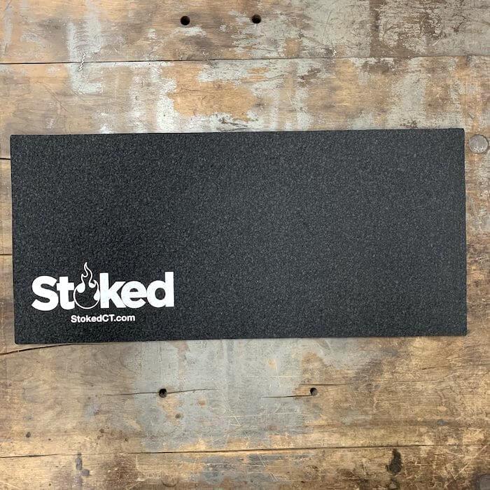 Black mood mat on a wooden background; white Stoked logo in bottom left corner, includes stokedCT.com