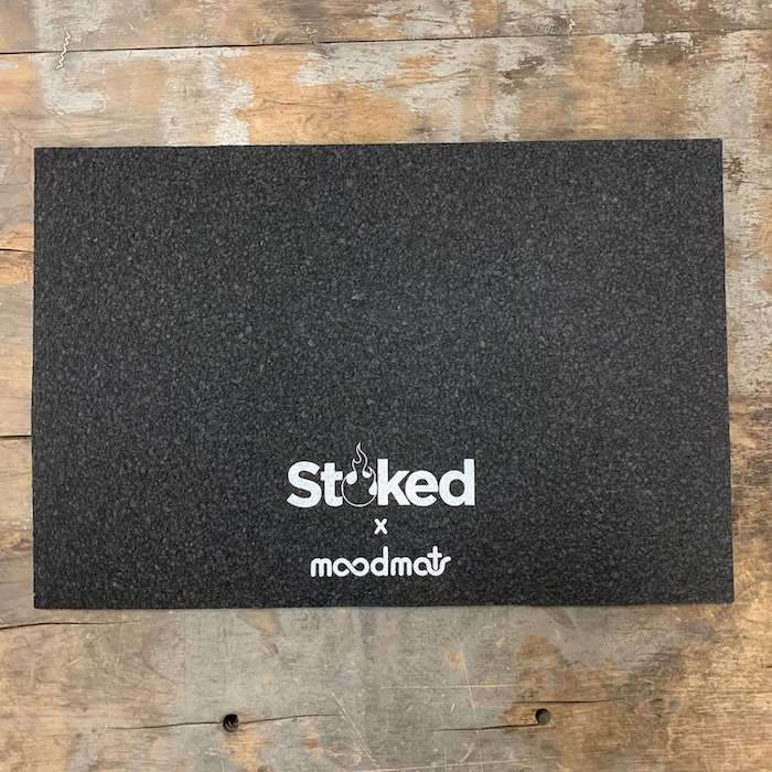 Stoked 12x18 inch mood mat on wood background with Stoked x moodmats logo center bottom