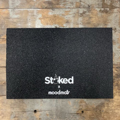 Stoked 12x18 inch mood mat on wood background with Stoked x moodmats logo center bottom