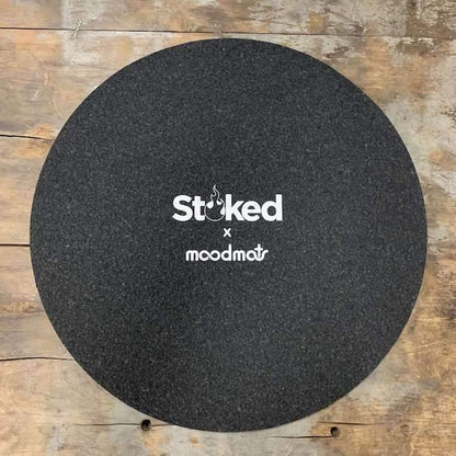 Stoked 17 inch circular mood mat on wood background with Stoked x Moodmats logo centered in white
