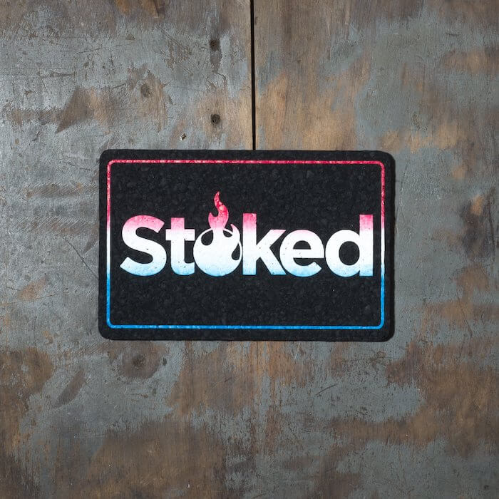 Stoked 8x5 inch black mood mat on a wood background. Stoked logo and outer outline are red fading to white fading to blue