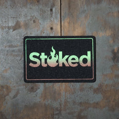 Stoked 8x5 inch black mood mat on a wood background. Stoked logo and outer outline are green fading to brown.