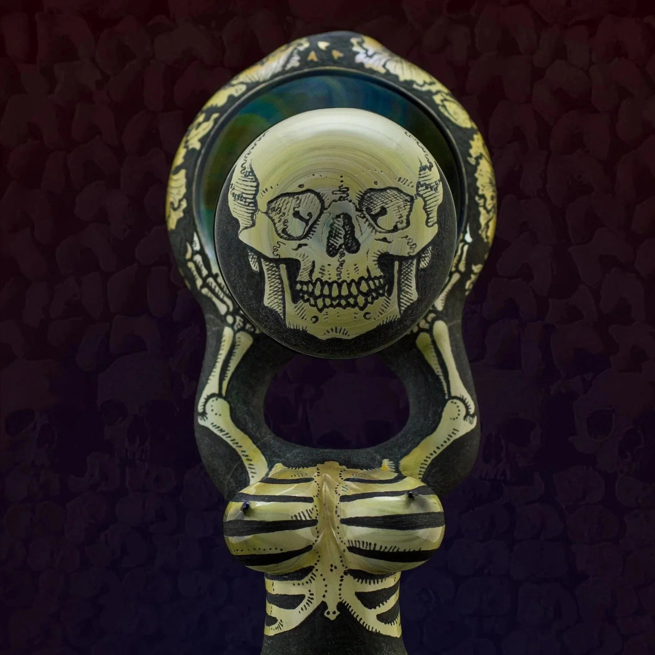 Hand-blown glass pipe with intricate skull and skeleton design on dark background