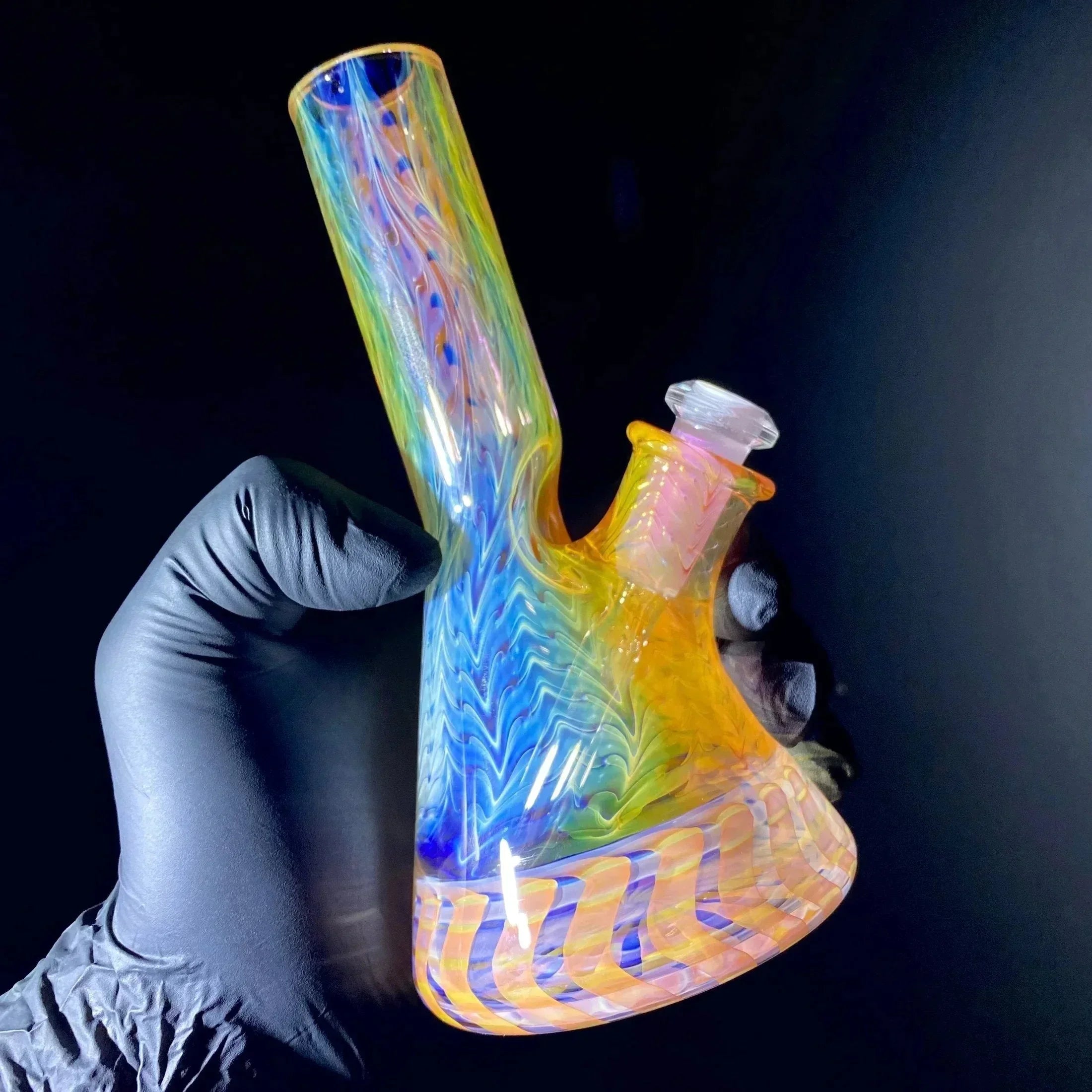 Hand holding a colorful rainbow glass water pipe with vibrant swirling patterns on black background