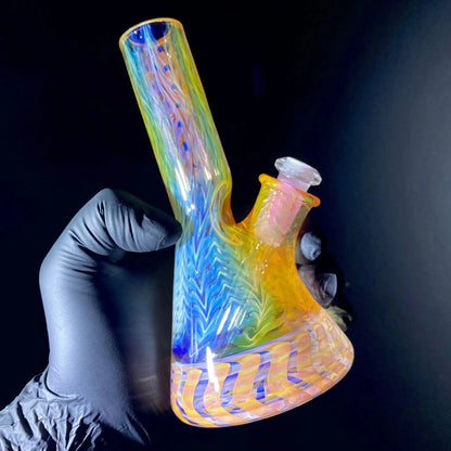 Hand holding a colorful rainbow glass water pipe with vibrant swirling patterns on black background